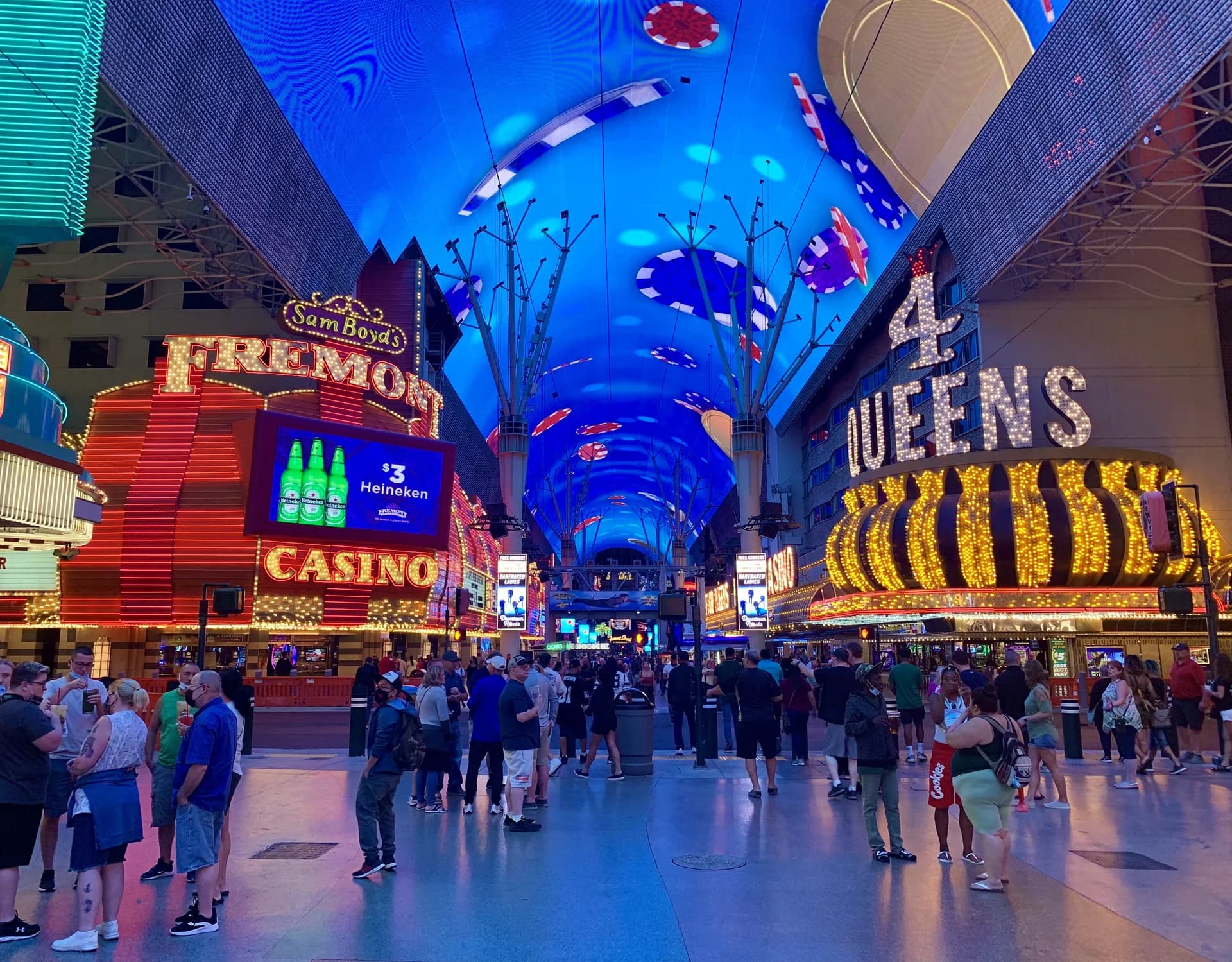 Crowds under the blue Viva Vision canopy, framed by illuminated Fremont Casino and Four Queens signs in downtown Las Vegas.