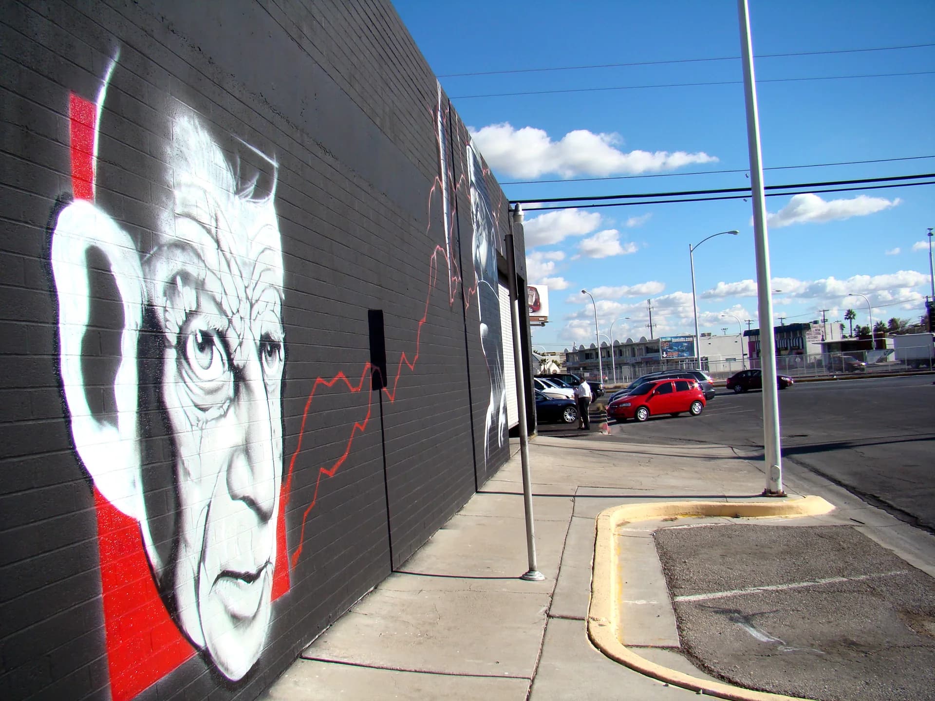 A black-and-white face mural, outlined by a red stripe, on a sidewalk wall in the Las Vegas Arts District.